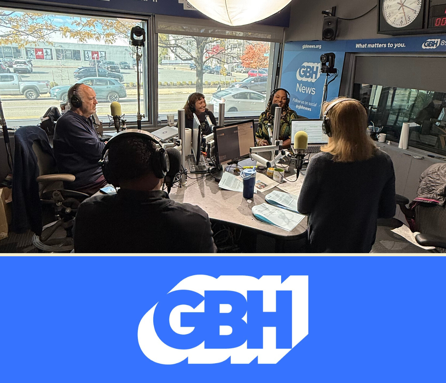 Four people sit around microphones in a radio studio, engaged in discussion. Headphones, computers, and papers are on the table. Large windows show cars and trees outside. Below is a blue banner with a white GBH logo.