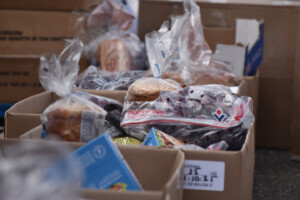 Close-up of cardboard boxes filled with packaged food items, including bread, grapes in plastic bags, and other groceries, ready for distribution.