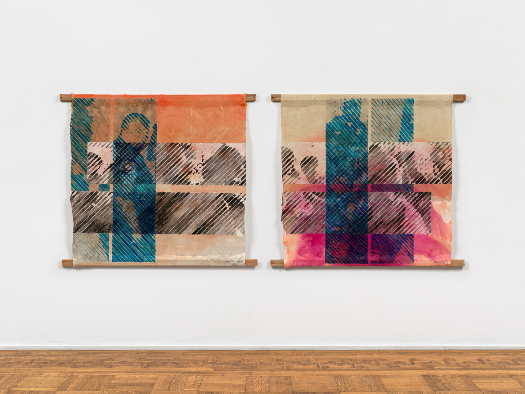 Two abstract textile artworks hang side by side on a white wall. Each features bold, intersecting lines and blocks of blue, orange, pink, and brown, resembling human silhouettes, mounted on wooden rods.