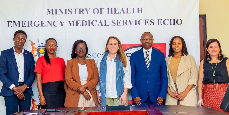 Seven people standing and smiling in front of a Ministry of Health Emergency Medical Services ECHO banner in a conference room.