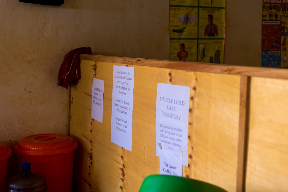 A wooden partition with printed notices attached, orange bins below, and colorful educational posters on a yellow wall in the background.